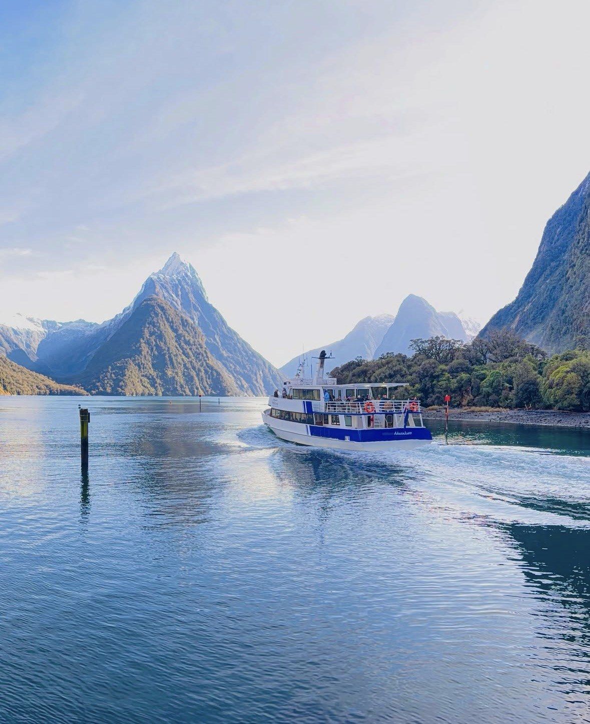 Cruise boat leaving the wharf past Mitre Peak in pale morning light