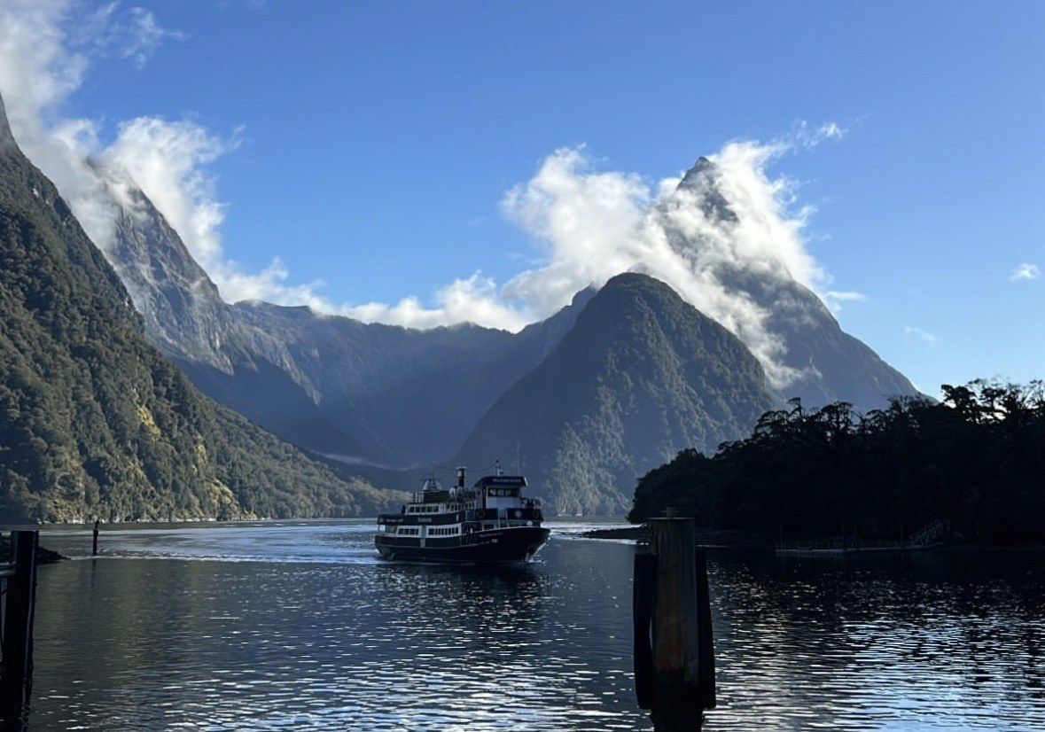 Cruise boat passing mountains wrapped in wisps of cloud, clear sky