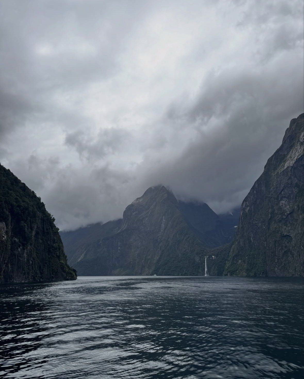 Dark peaks and distant waterfall under heavy cloud over Milford Sound