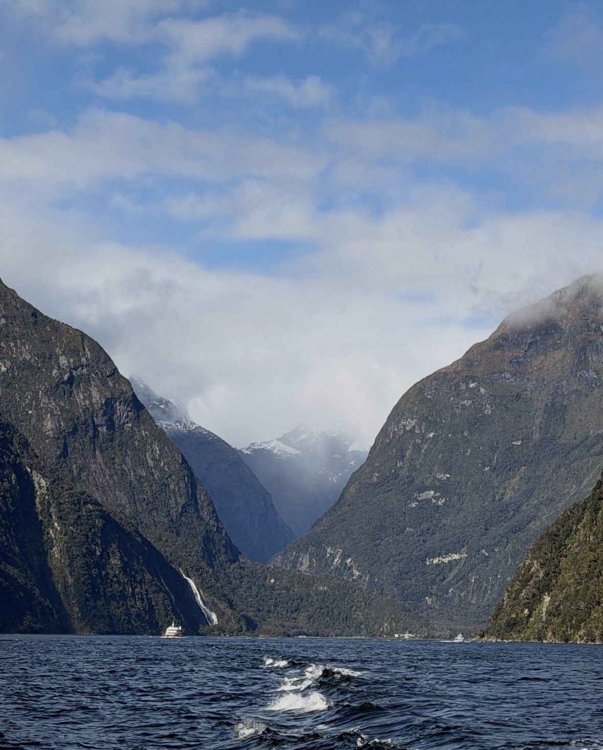 Sunlit valley, waterfall and small cruise boats deep inside Milford Sound
