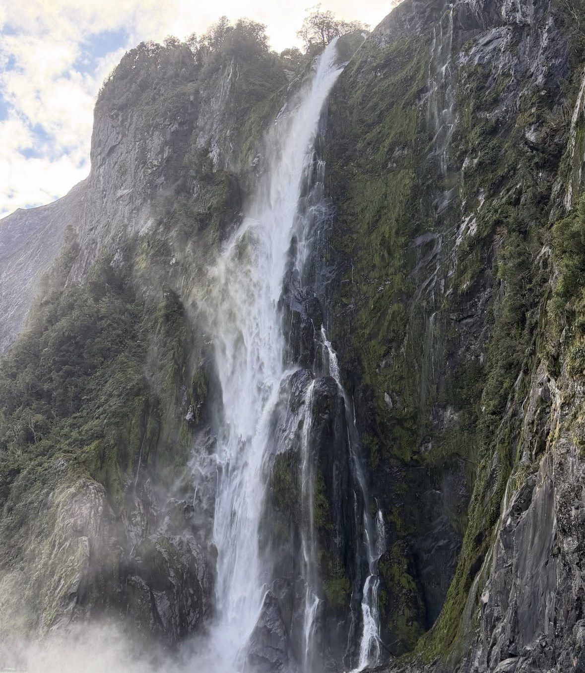 Waterfall plunging past mossy rock walls at Milford Sound in daylight